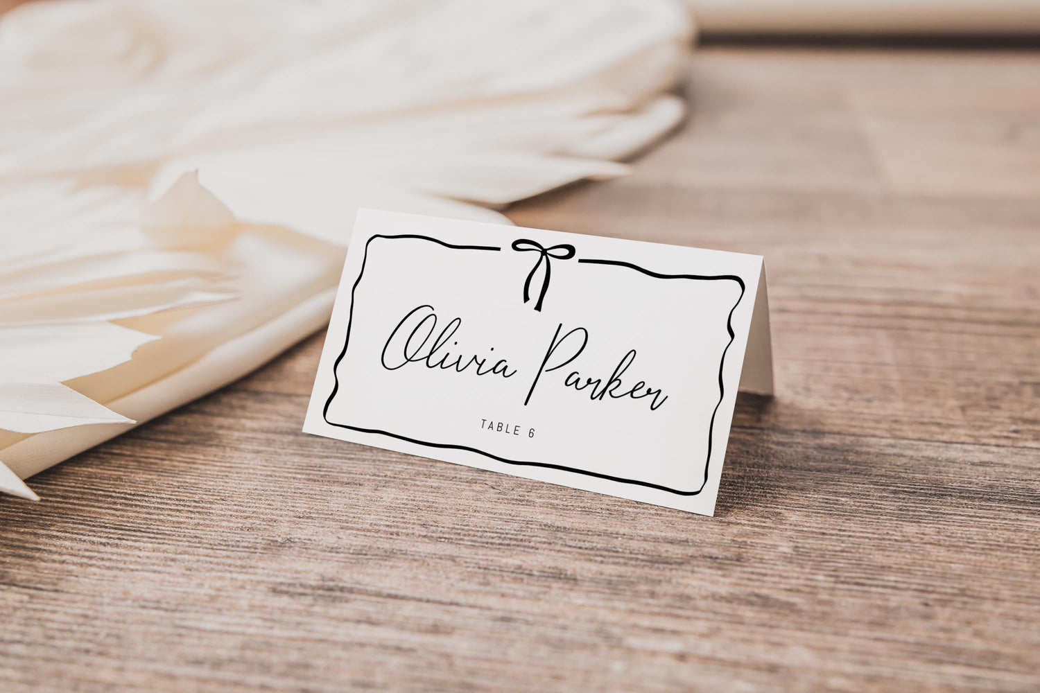 place card with simple black bow and ribbon like frame surrounding name and table number.  modern minimalist editable template