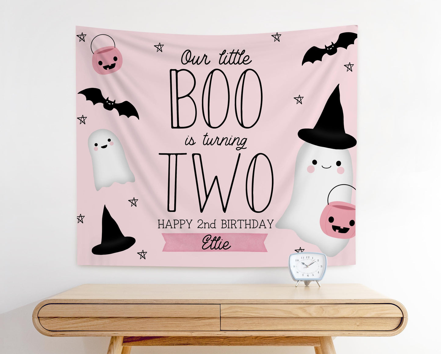 pink and black girl 2nd birthday backdrop for halloween theme.  graphics of bats, ghosts, pumpkins and witches hats.  Pale pink background in modern playful design reads "Our little BOO is turning TWO, Happy 2nd Birthday Ellie"