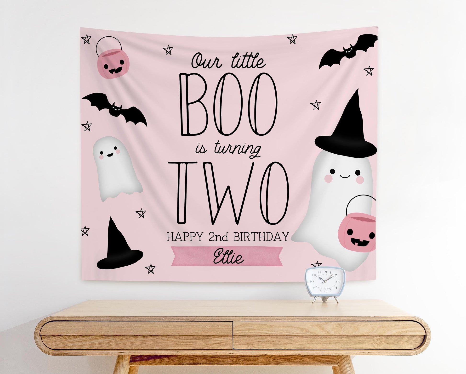 pink and black girl 2nd birthday backdrop for halloween theme.  graphics of bats, ghosts, pumpkins and witches hats.  Pale pink background in modern playful design reads "Our little BOO is turning TWO, Happy 2nd Birthday Ellie"