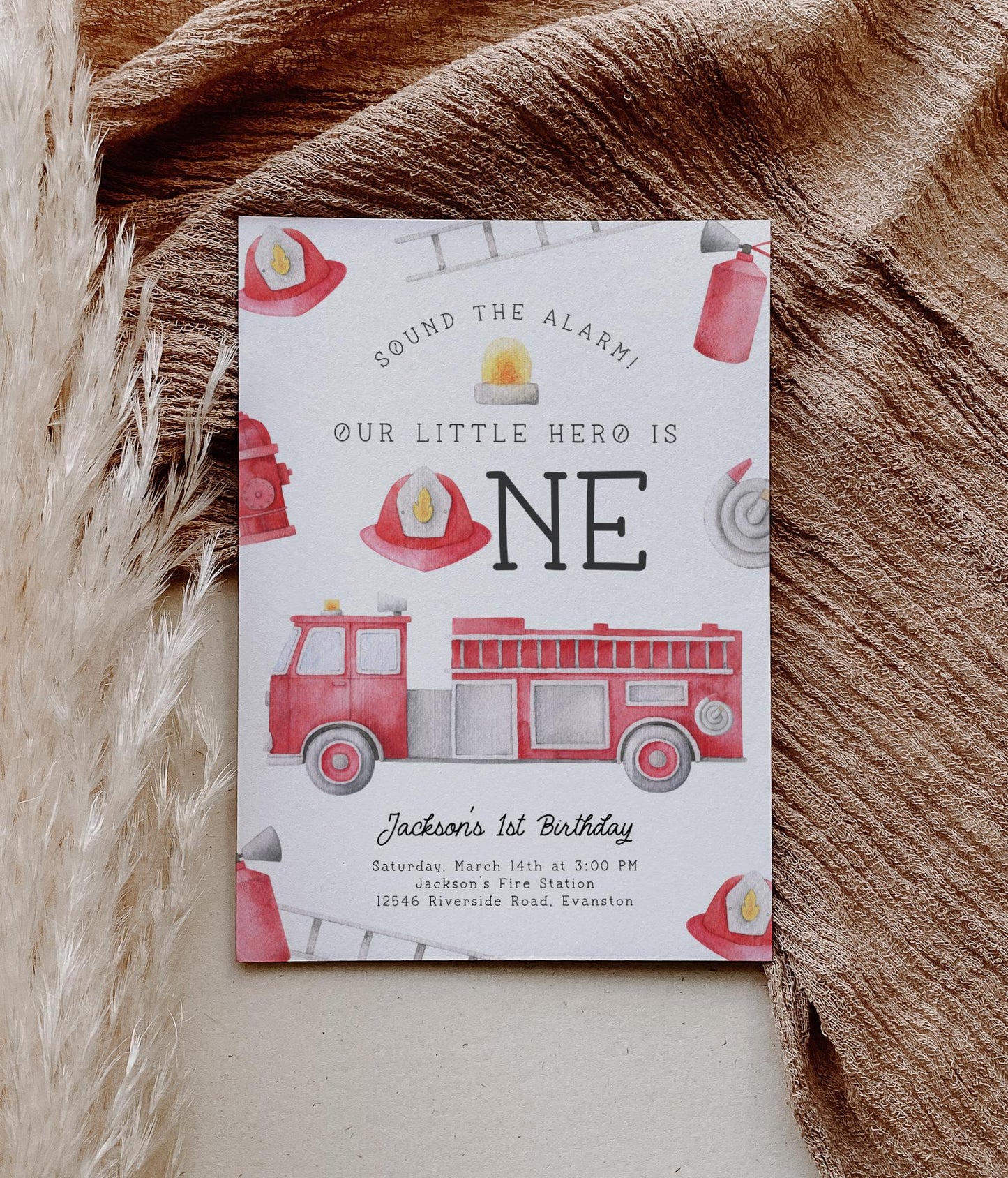 firetruck first birthday party invitation with playful watercolor graphics of firetruck, hose, hat, ladder, hydrant, extinguisher and siren light.  Reads "sound the alarm! Our little hero is ONE".  A fireman's hat is used in place of the "o" in ONE.