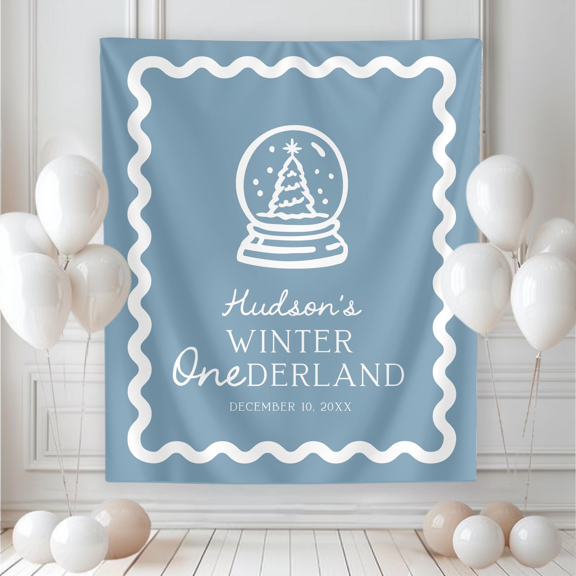 large backdrop hanging on wall.  blue with white graphics and wavy border.  christmas tree in snow globe and reads "hudson's winter ONEderland" with date of party below.  white balloons rest near both sides of banner