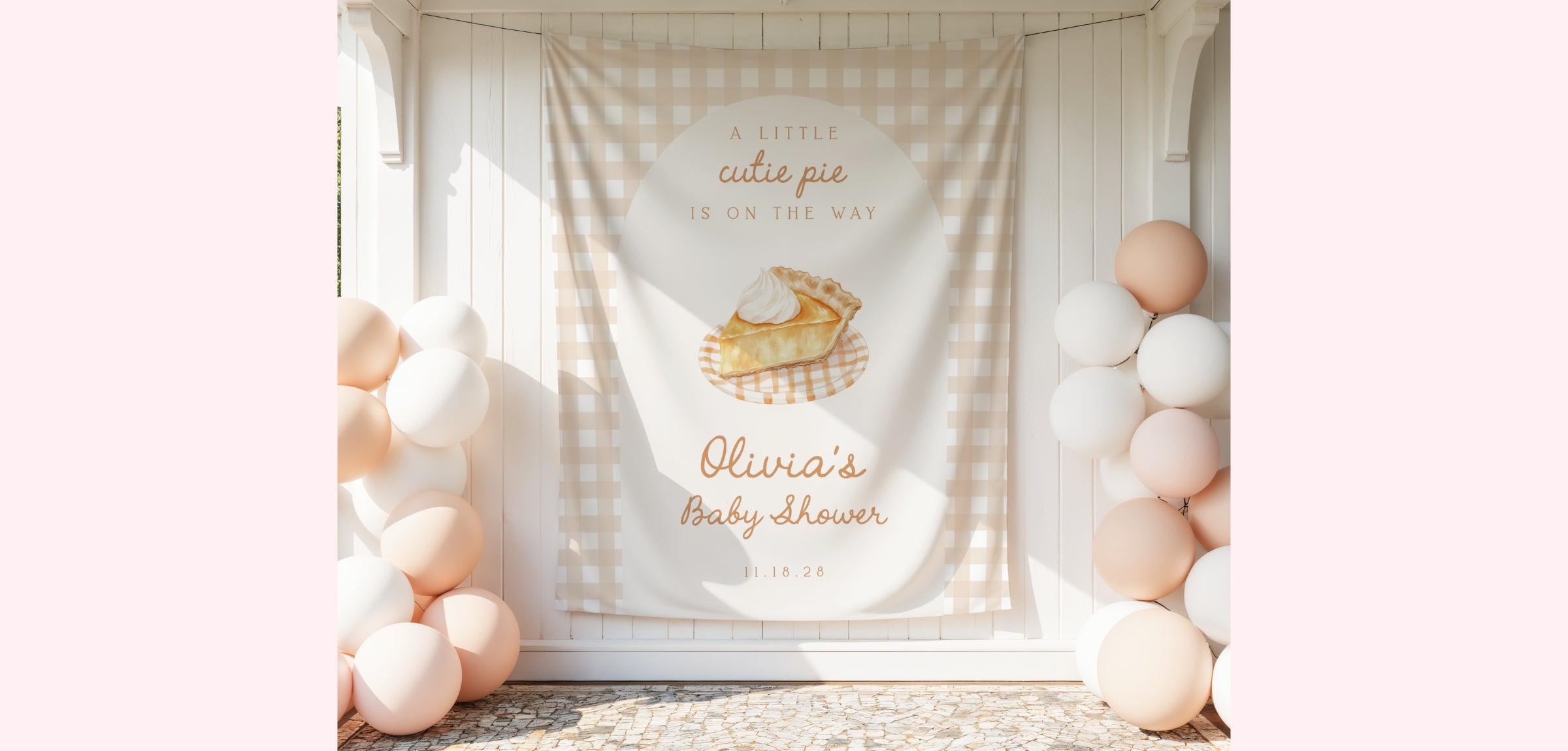 A custom baby shower backdrop banner featuring a gingham pattern, a watercolor illustration of a basket of pie, and personalized text reading 'Olivia's Baby shower'. The banner is displayed in a styled setting with pastel pink and white balloons on either side.