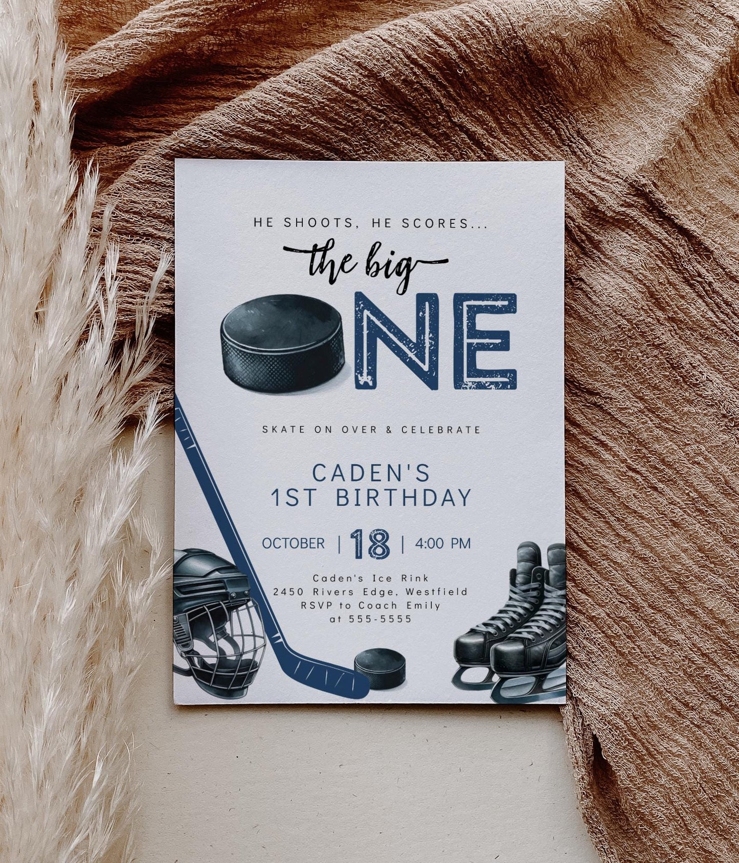 Hockey themed first birthday invitation with ‘he shoots he scores the big ONE’ text and mask, hockey stick, puck and skates graphics.