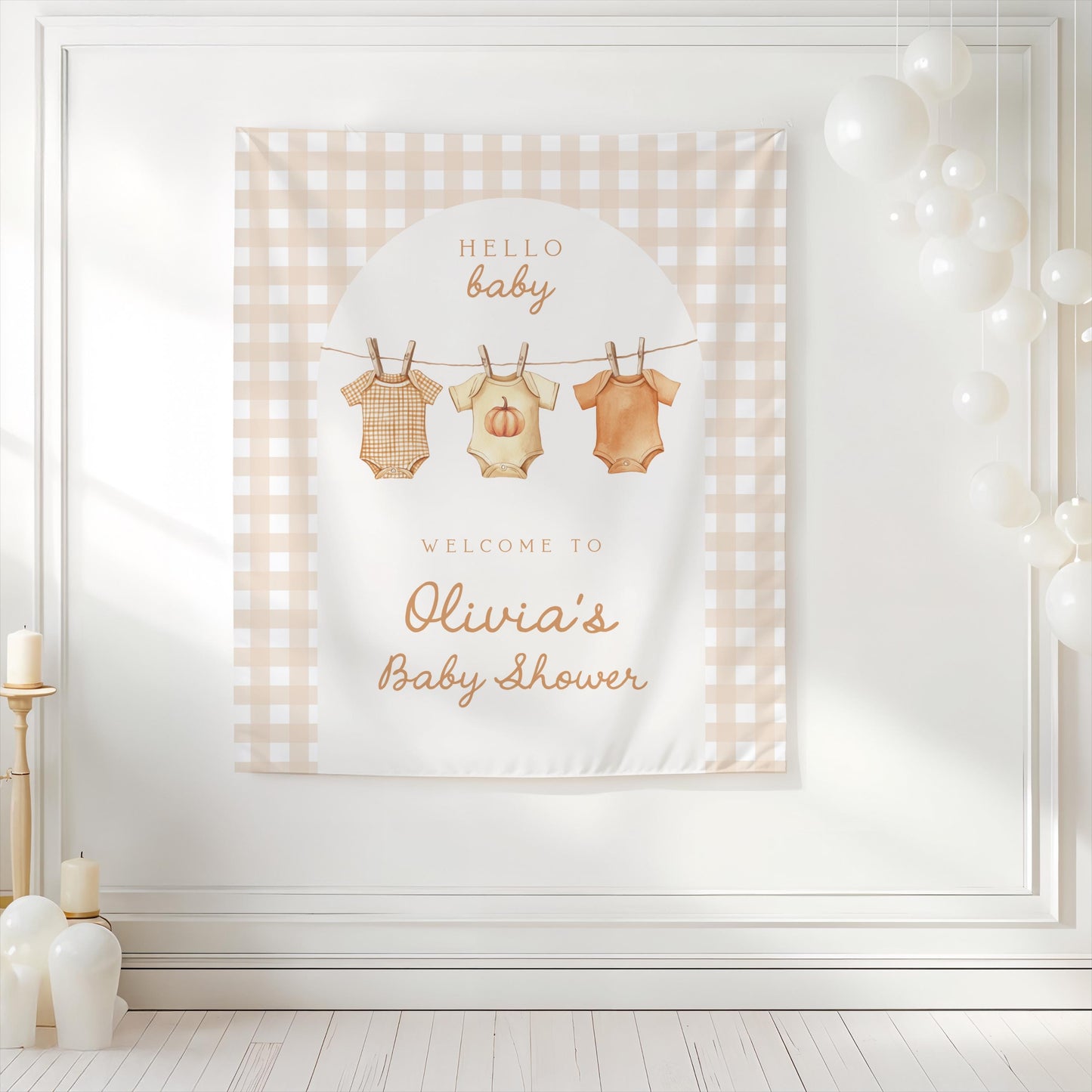 Neutral gingham baby shower backdrop with pumpkin onesies hanging on clothesline design, personalized with “Welcome to Olivia’s Baby Shower” and background decorated with white balloons.