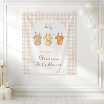 Neutral gingham baby shower backdrop with pumpkin onesies hanging on clothesline design, personalized with “Welcome to Olivia’s Baby Shower” and background decorated with white balloons.