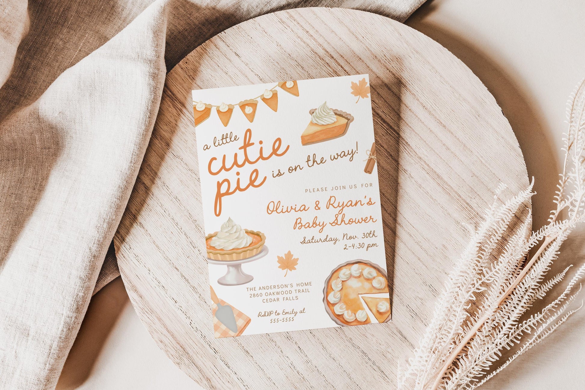 Editable Cutie Pie fall baby shower invitation featuring hand-drawn pumpkin pies and orange lettering, styled on a wooden tray with linen fabric and dried fall foliage.