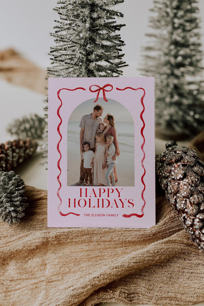 pink and red christmas photo card with bow and ribbon outline, reads "happy holidays, the ellison family"