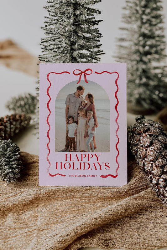pink and red christmas photo card with bow and ribbon outline, reads &quot;happy holidays, the ellison family&quot;