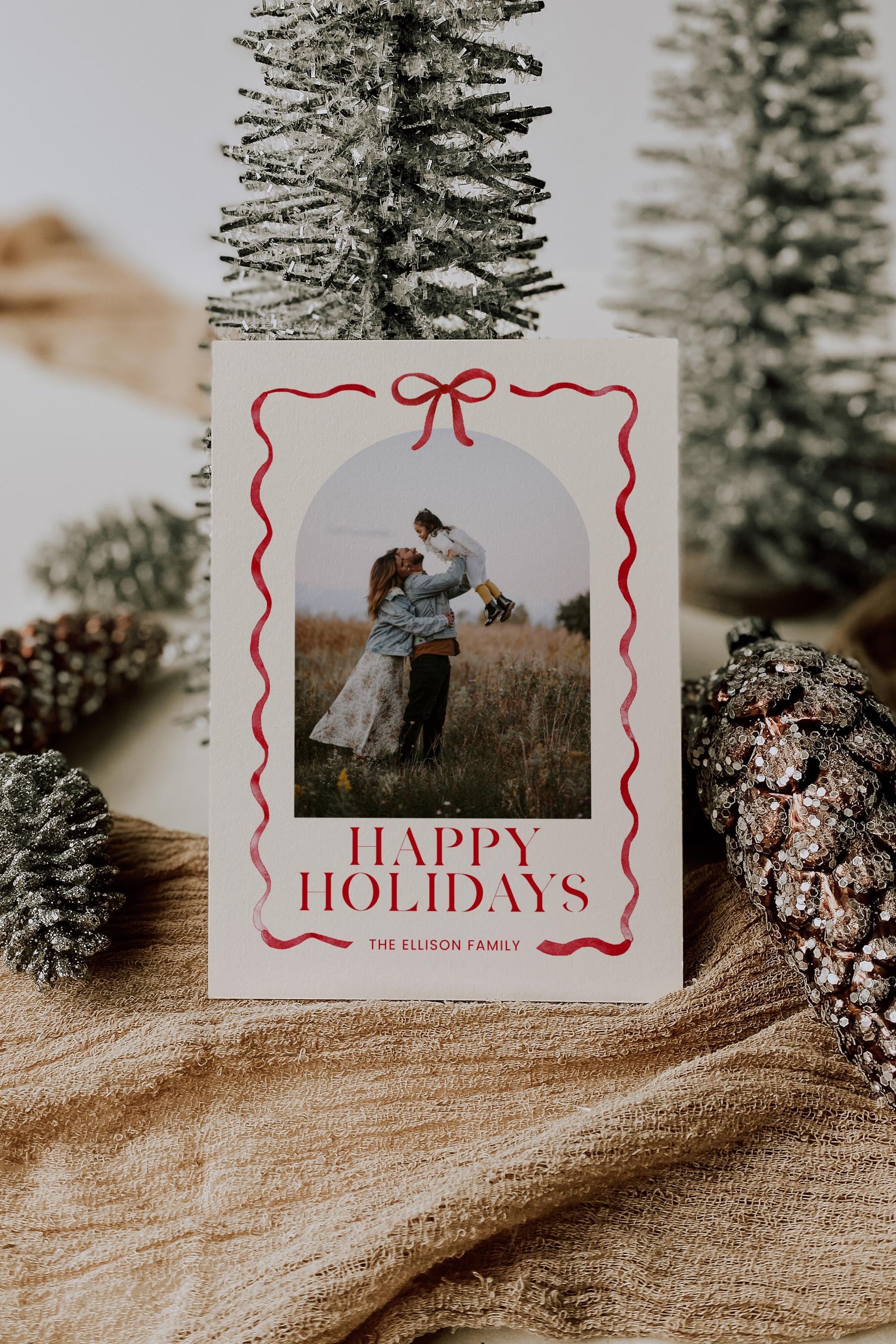 holiday photo card natural beige cream background with red bow and ribbon surrounding photo.  reads &quot;happy holidays, the ellison family&quot;