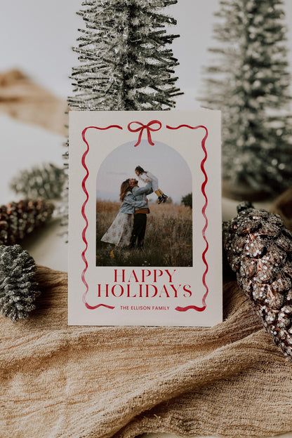 holiday photo card natural beige cream background with red bow and ribbon surrounding photo.  reads &quot;happy holidays, the ellison family&quot;