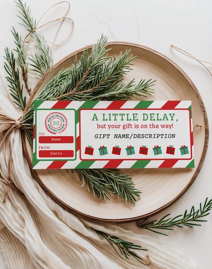 Editable Christmas gift delay certificate template in red and green stripes displayed on a holiday tray with pine branches; printable Canva late gift note