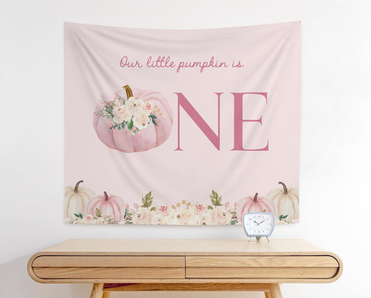 Boho aesthetic floral pumpkin first birthday backdrop with blush pumpkins, flowers, and text “Our little pumpkin is ONE&quot;