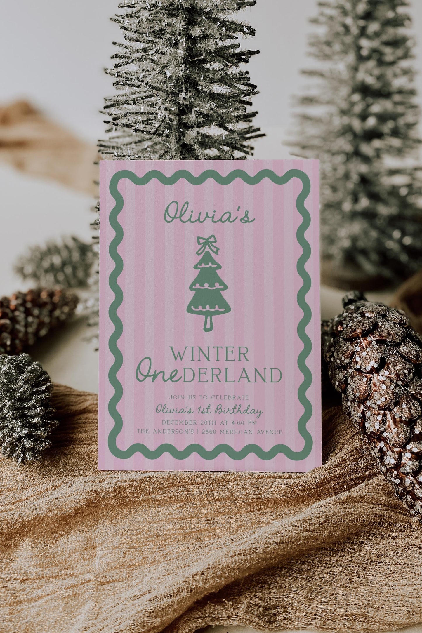 pink green winter onederland first birthday invitation with pink stripe background a sage green wavy border.  graphic of christmas tree with bow on top.